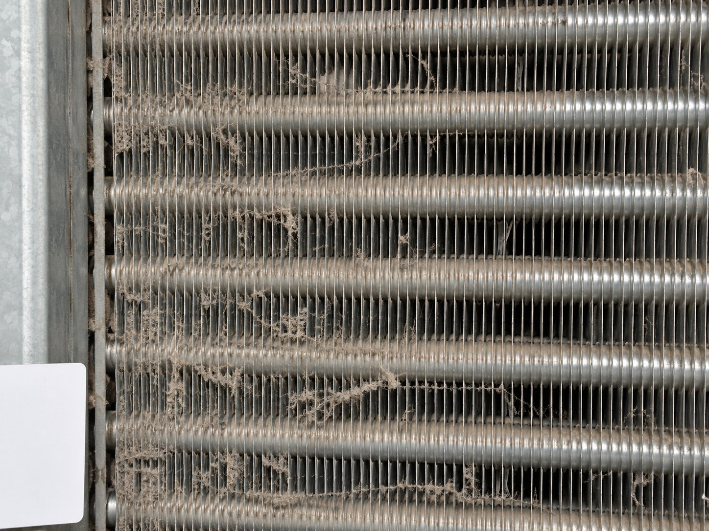 Close view of straight industrial heat exchanger fins with light dust and lint in some air passages
